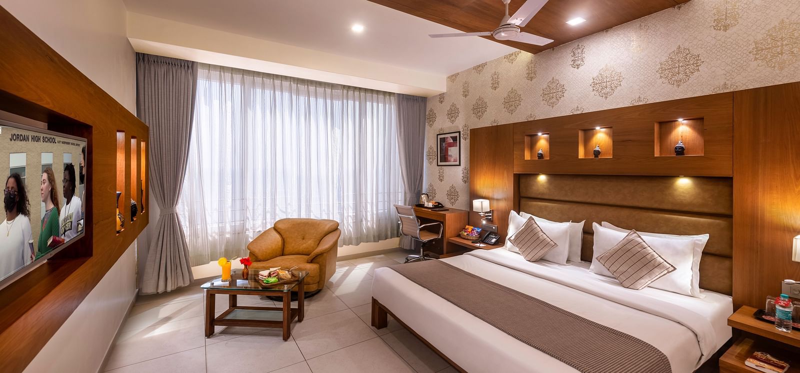 A well-appointed hotel room  featuring a bed, seating area, workspace, and a wall-mounted TV.