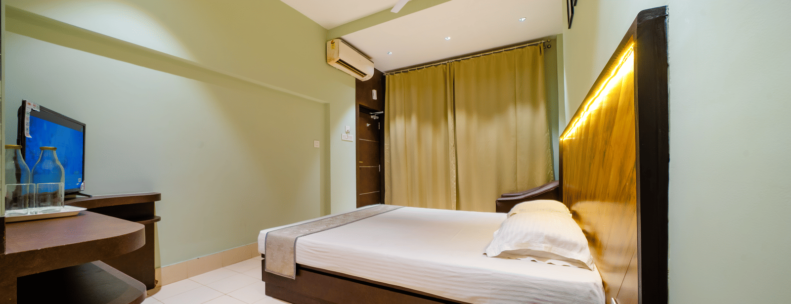 Hotel bedroom with a double bed, light green walls, and a flat-screen TV on a stand - Hotel Dolphin Puri