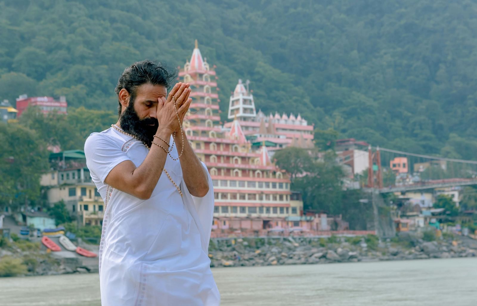 An image of a person praying in front of ganga river and there is a temple behind him