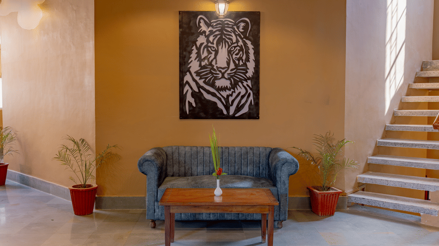 A seating area at Estherea Bagh, Ranthambore, with a sofa, a tiger portrait on the wall, and a wooden staircase next to tan-colored walls.