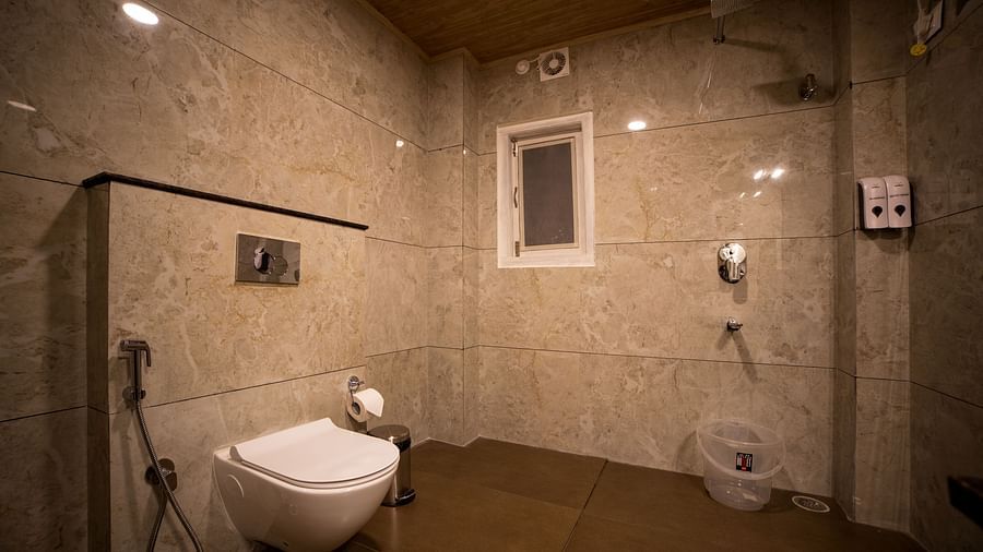 Modern hotel bathroom with beige marble walls, wall-mounted toilet, handheld bidet spray, and an open shower area with basic fixtures - Yashshree Pelling Chekhim Retreat.