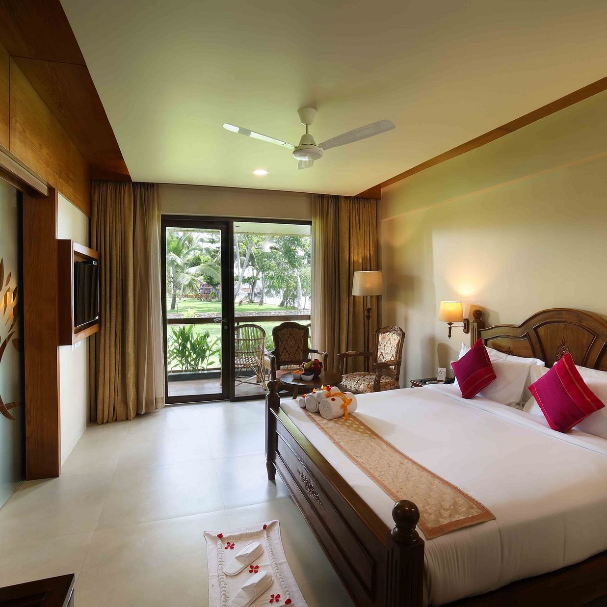 Lake View Suite in Uday Backwater Resort features a plush wooden bed with fresh linen and ribbon-tied towels, complemented by a cosy seating area beside the balcony and a lamp in the corner