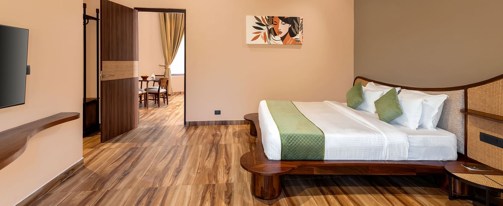 Luxury Villa with Sitout featuring a king size bed with a green-accented throw and headboard, complemented by wooden furniture and a view into an adjacent room at The Qualia Resort Club & Brewery, Udaipur.