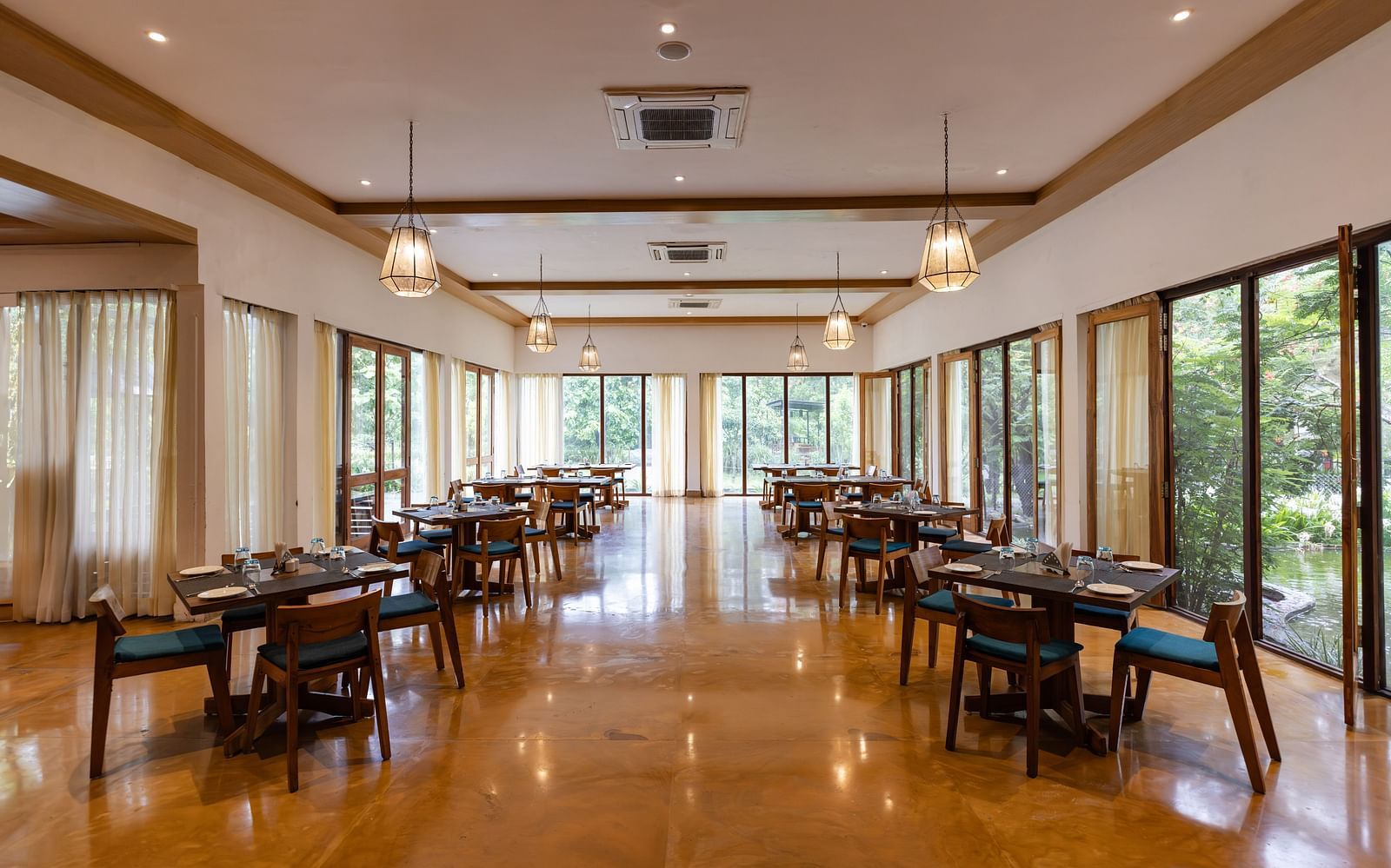 Seating arrangement in Azrak Restaurant at Saraca Resort & Spa Corbett with wooden flooring and wooden panelling on the ceiling alongside large French windows bringing in lots of light