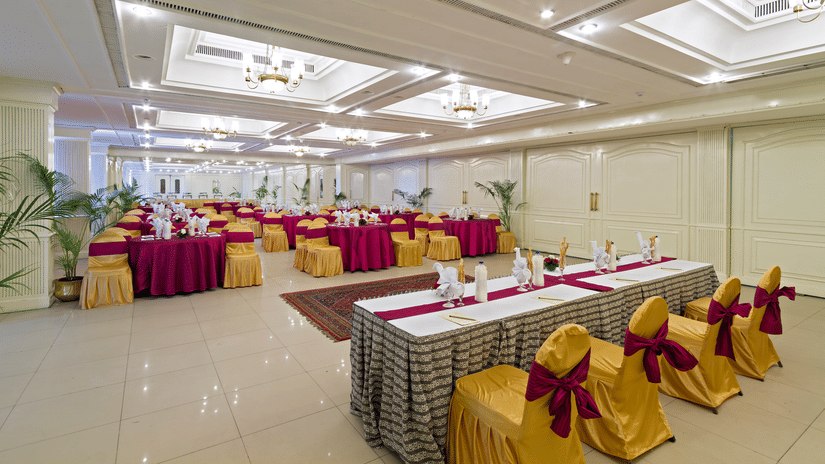 A bright event space with tables arranged for a function, decorated with red and yellow fabric on the chairs and tables - Clarks Avadh, Lucknow