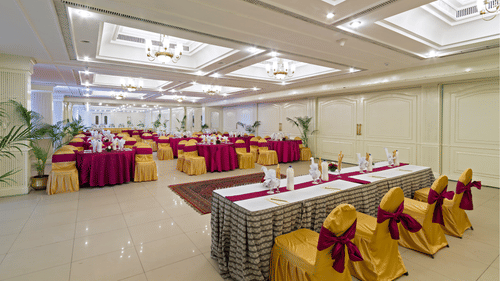 A bright event space with tables arranged for a function, decorated with red and yellow fabric on the chairs and tables - Clarks Avadh, Lucknow