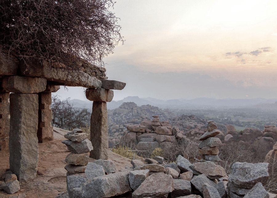 Ancient stone temple ruins on a hill overlooking the rugged, rocky valleys of Hampi.