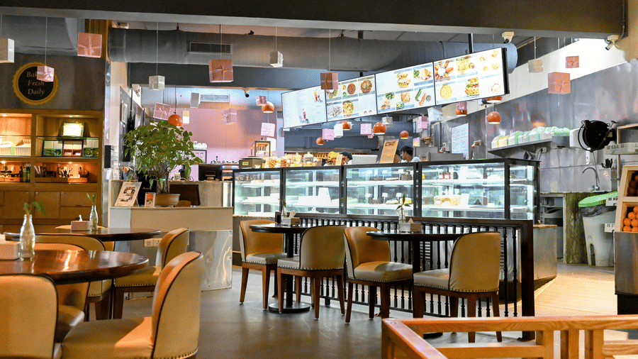 A cosy indoor dining area of Zolocrust restaurant with tables and chairs in front of an open kitchen where food is displayed at Clarks Amer, a hotel near Jaipur airport.