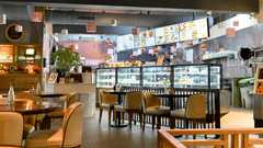 A cosy indoor dining area of Zolocrust restaurant with tables and chairs in front of an open kitchen where food is displayed at Clarks Amer, a hotel near Jaipur airport.