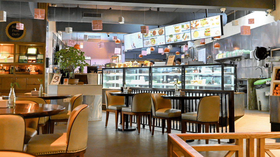 A cosy indoor dining area of Zolocrust restaurant with tables and chairs in front of an open kitchen where food is displayed at Clarks Amer, a hotel near Jaipur airport.