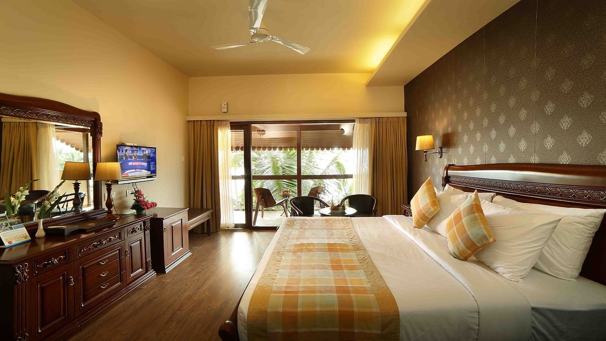 The Ocean Breeze Suite at Uday Samudra Leisure Beach Hotel offers a king size bed, a dressing table, a television, and a balcony as the daylight makes its way in through the large windows