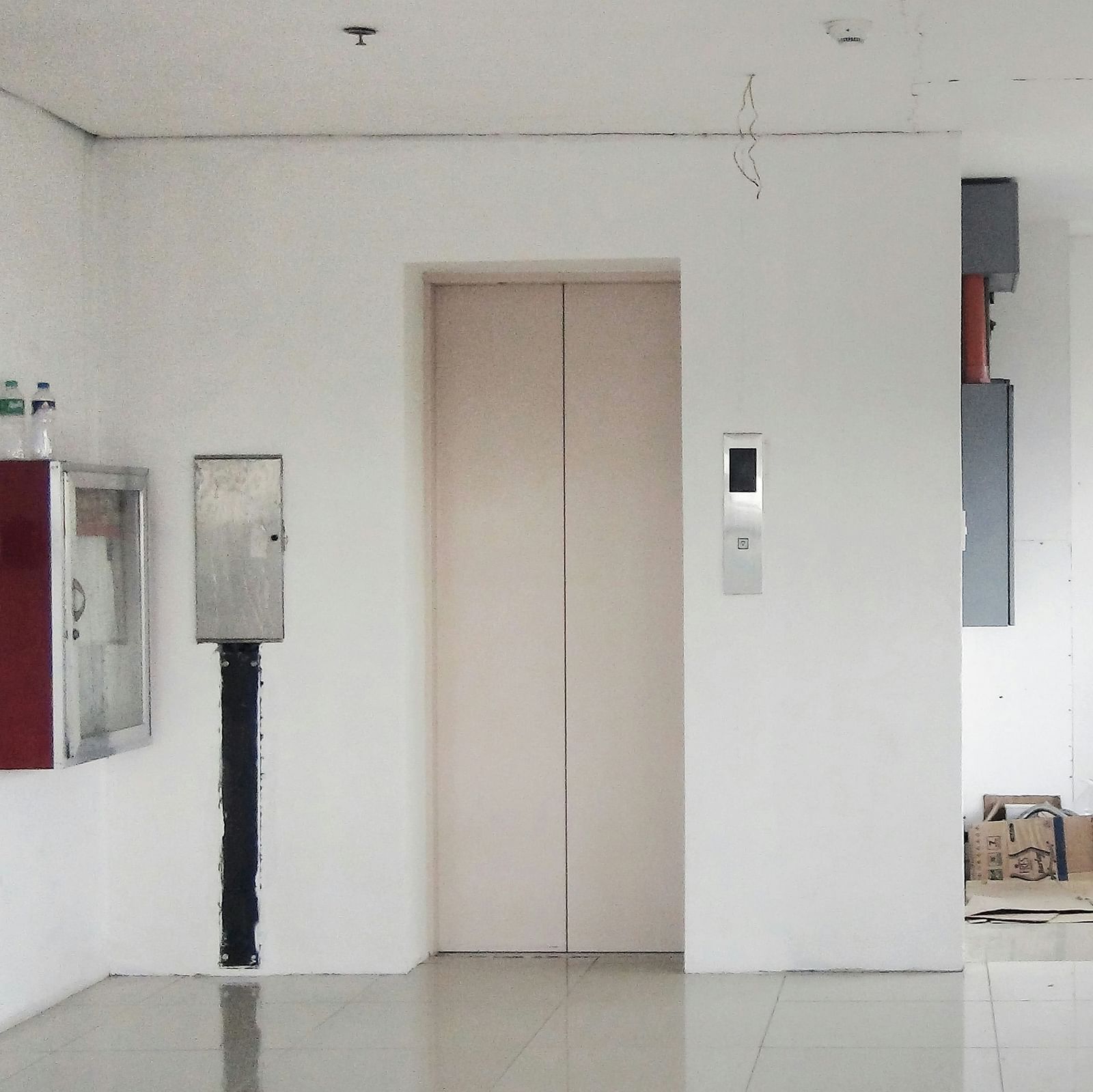 A landscape image showing the entrance of an elevator, with a hint of the emergency safety measures of the building, in a white walled hall.