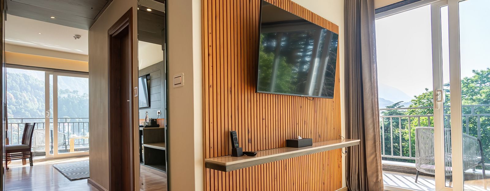 An image of a Suite with a flat screen TV, a full length mirror, and an expansive glass door leading to the balcony - The Belvedere Himalayan Retreat, McLeodganj
