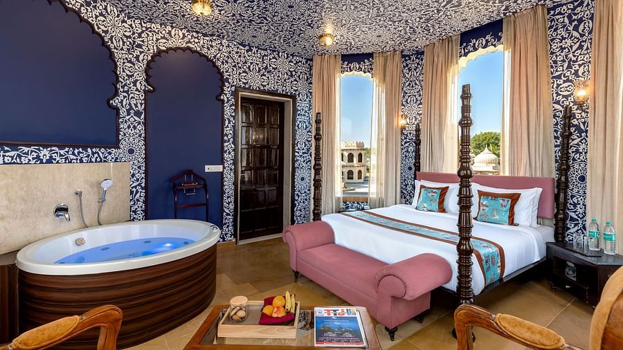 Heritage-style bedroom with ornate blue interiors, canopy bed, and in-room hot tub at Kesar Bagh Palace.