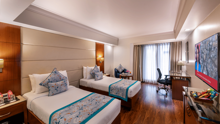 Deluxe twin bedroom with wooden flooring, flat screen TV, sitting area and bright lighting Lords Plaza Jaipur.