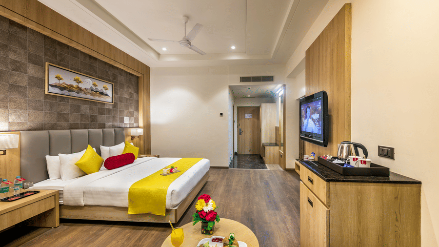 A premium room in Lords Inn Somnath with modern interiors, featuring a neatly made double bed, lounge chair, entertainment unit, and a table set with refreshments.