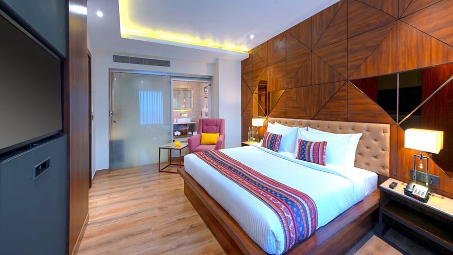 An image of a bedroom with double size bed, bedside table next to it which has a lamp and a telephone on it, and at one corner there is a sofa and tea table - Golden Tulip, Agra