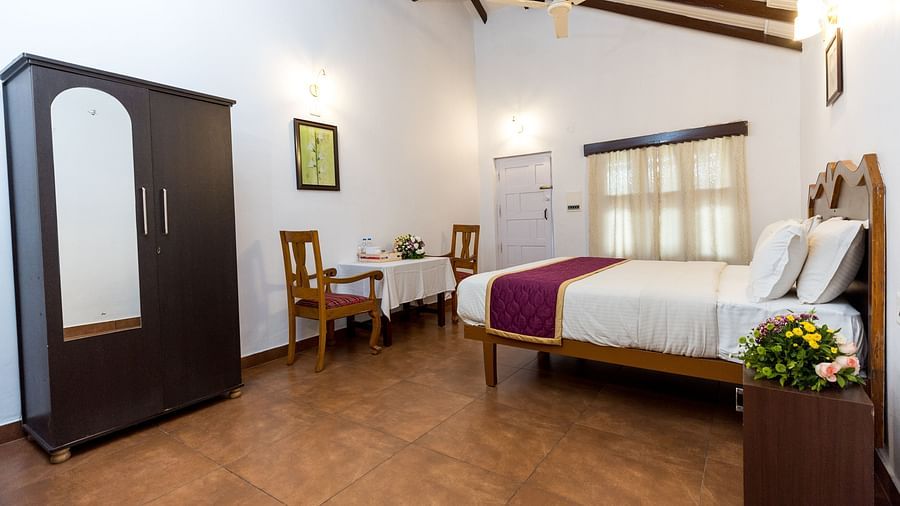 A king bed opposite chairs & table at Deluxe Double room in Capitol Village Resort, Madikeri