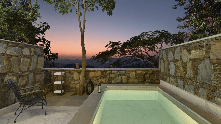 Plunge Pool Suite with Jacuzzi at Fateh Safari Suites, Kumbhalgarh featuring a small pool, chair next to it, a wine bottle with glass, towel rack, and a view of sunset.
