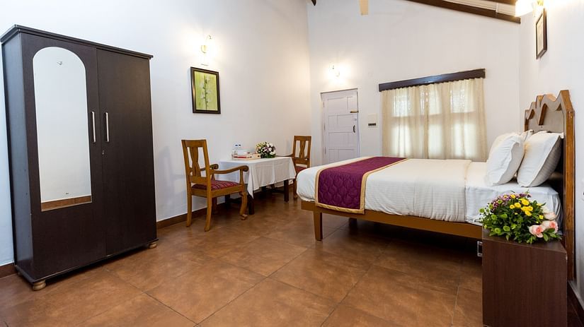 Capitol Village Resort, Madikeri Madikeri A king bed opposite chairs table at Deluxe Double room in Capitol Village Resort Madikeri