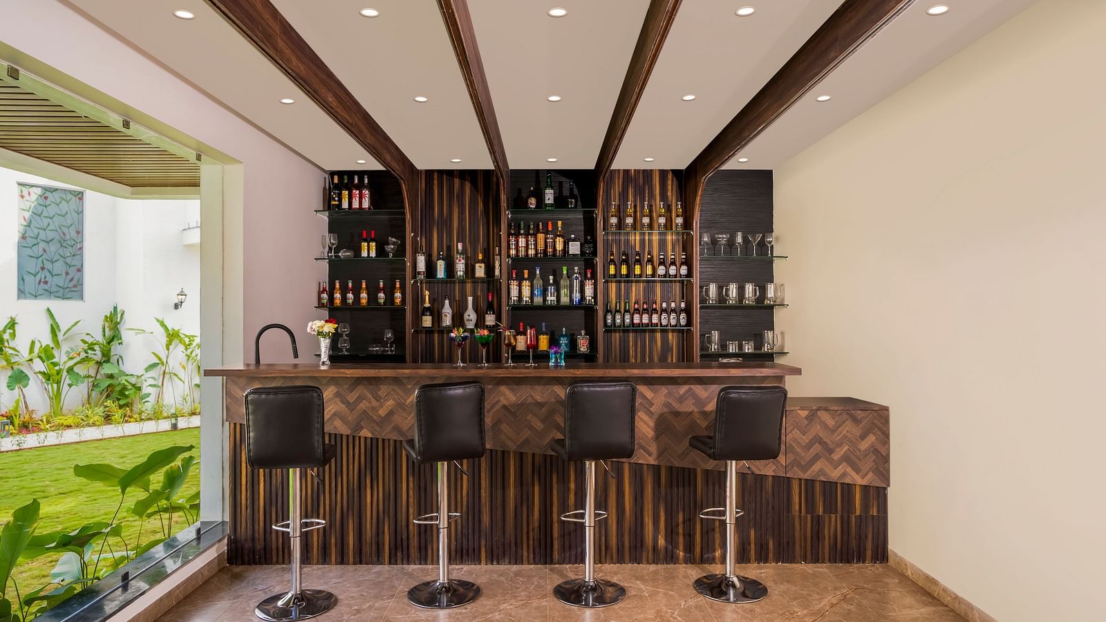 overview of the bar area with bat stools and a showcase with many bottles in it - The Tanisi Hotels & Resorts, Goa