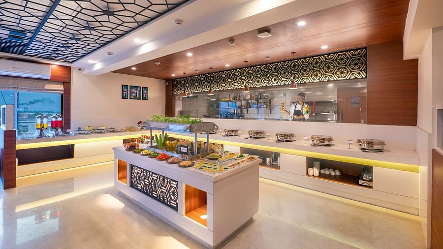 Buffet station with multiple serving counters and overhead lighting in restaurant setting - Lords Eco Inn Shapar Rajkot