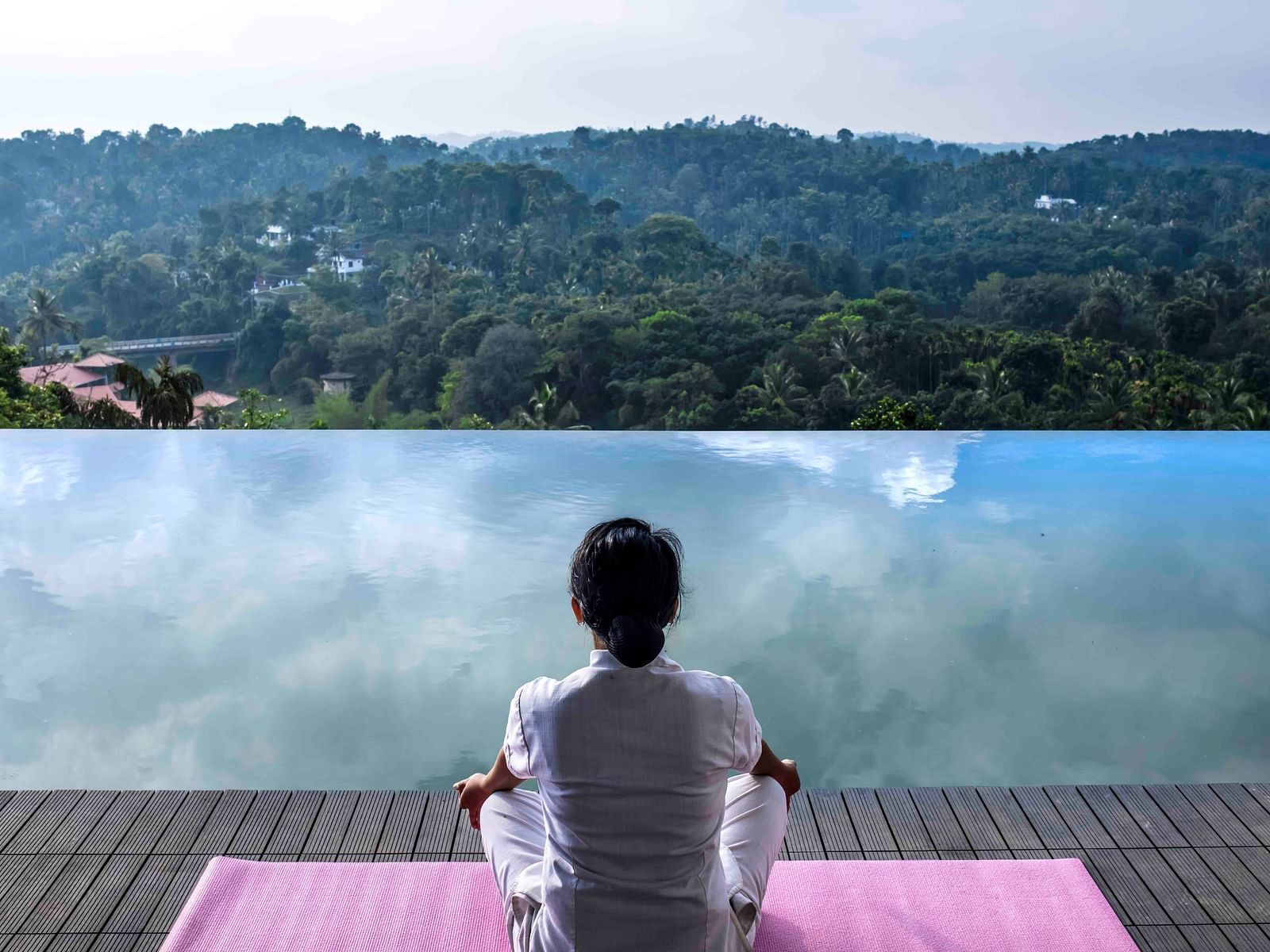 Image of the infinity pool with a women sitting by the pool and meditating.