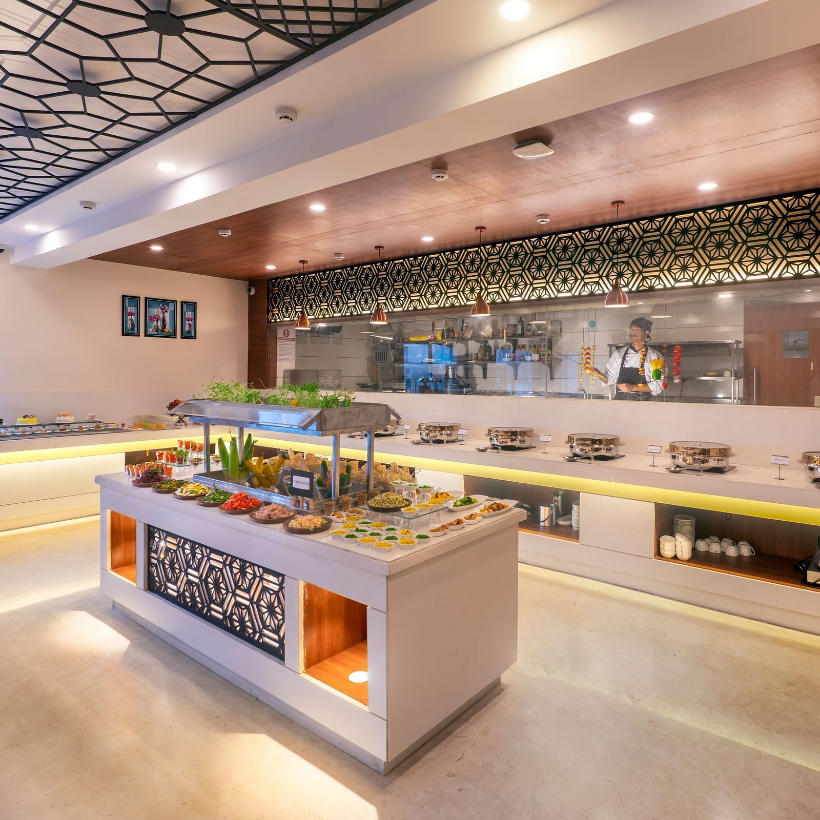 Buffet station with multiple serving counters and overhead lighting in restaurant setting at Lords Eco Inn Shapar Rajkot