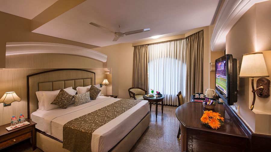 Hotel room with a king-sized bed, a decorative lamp, and a view of the outside through a window - Lords Inn Vadodara