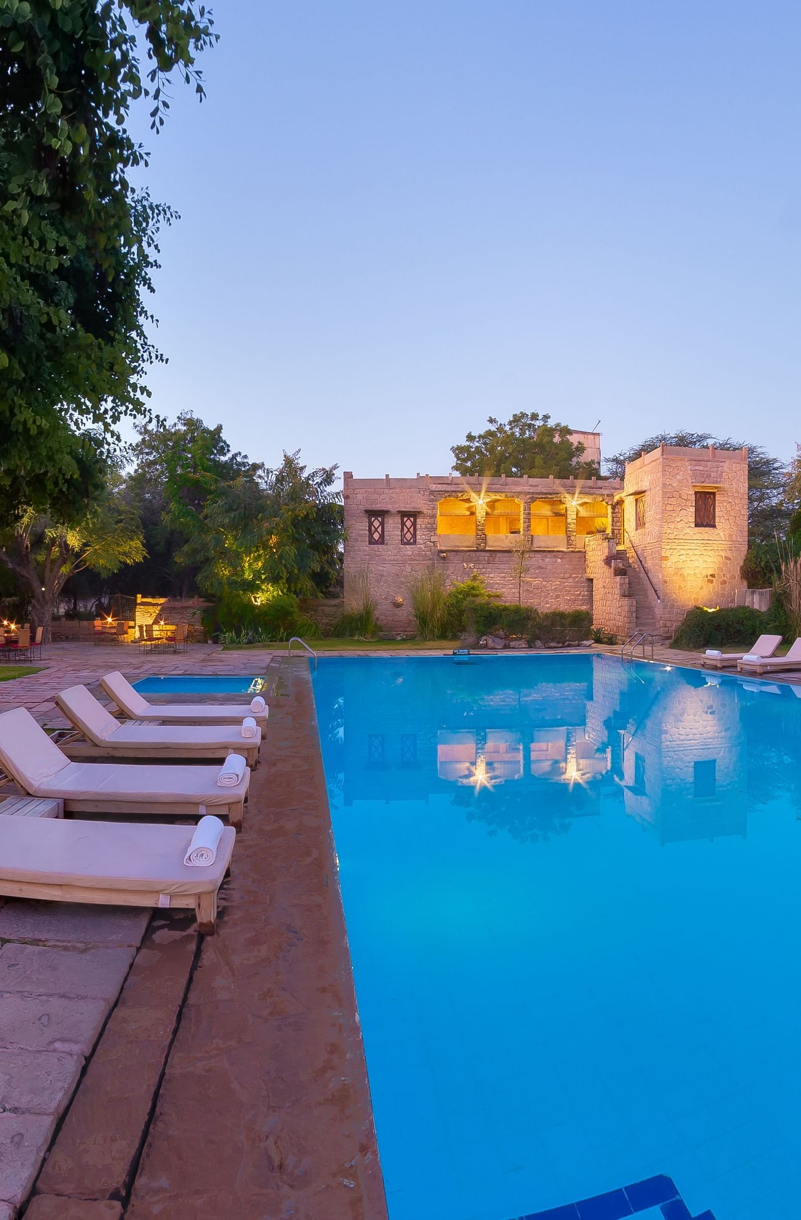 A tranquil swimming pool with loungers provides a refreshing oasis, reflecting the evening sky in its still waters - MANVAR Resort & Desert Camp