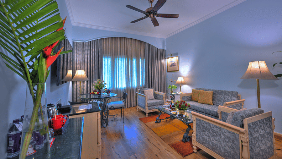 A room with a fan, chairs, sofa, a table, and windows. | Clarks Varanasi