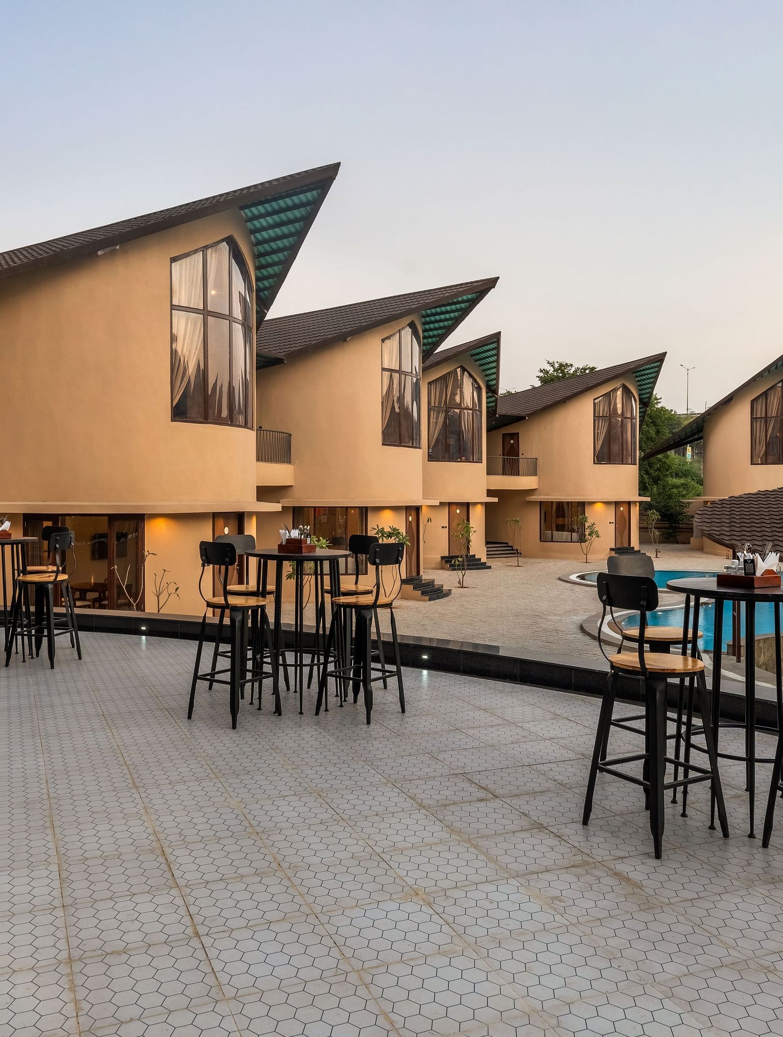 Exterior of Rhythm & Brews at dusk, showcasing modern architecture, outdoor seating areas, and a swimming pool at The Qualia Resort Club & Brewery, Udaipur.