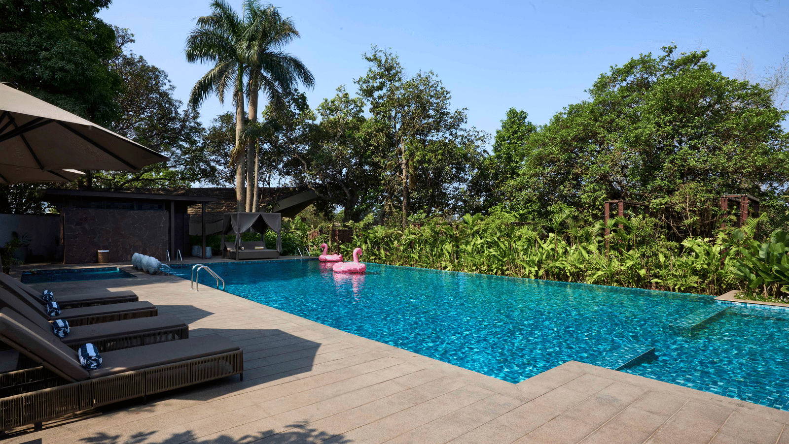 An outdoor swimming pool lined with sun loungers and surrounded by green trees at Athiva Resort & Spa, Khandala.