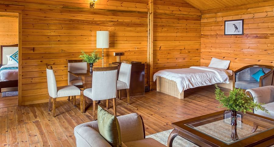 A spacious hotel suite at Digantaa Resort in Mukteshwar wooden walls, featuring a cozy seating area with a sofa and coffee table, plus a bed in the background