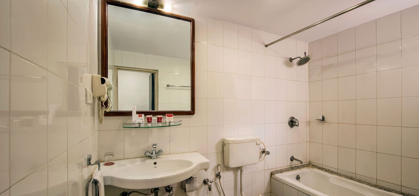 A modern bathroom at Lords Eco Inn Dahej, featuring a sink, toilet, bathtub with a shower and a mounted mirror.