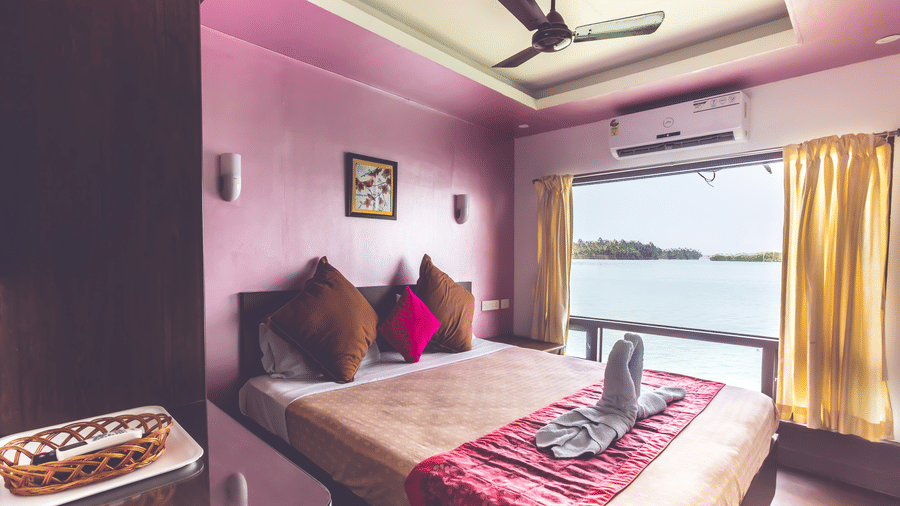 Room with pink and white walls, queen size bed, a wall frame & expansive window opening to the river view, at Paradise Lagoon Resort, Udupi.