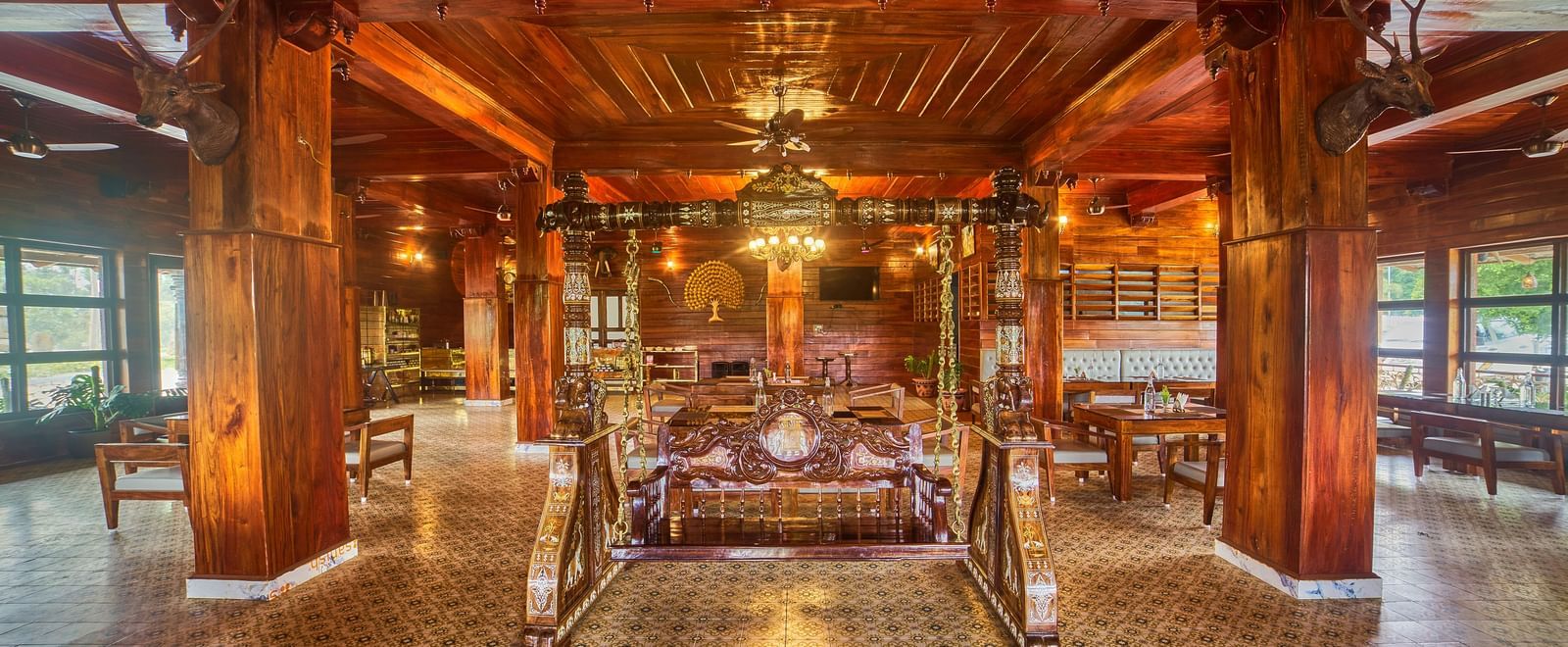 The richly decorated interior of a spacious common area or dining hall with polished wooden floors, intricately carved wooden ceilings and pillars, and ornate furniture, creating a luxurious ambience - Vintage Trails by Ilara