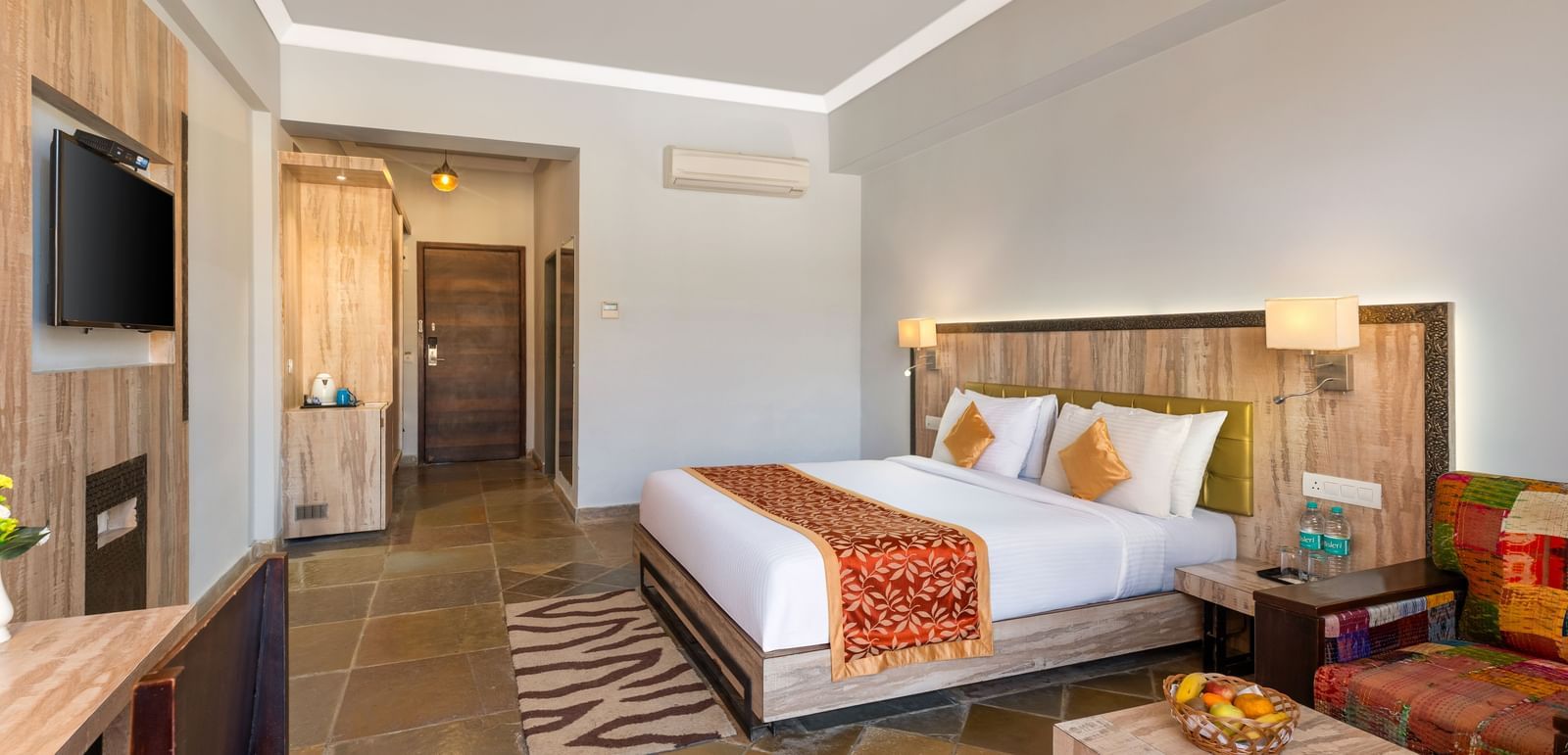 A hotel room with a bed, seating area, desk, TV, and a door leading to another room - Via Lakhela Resort & Spa, Kumbhalgarh