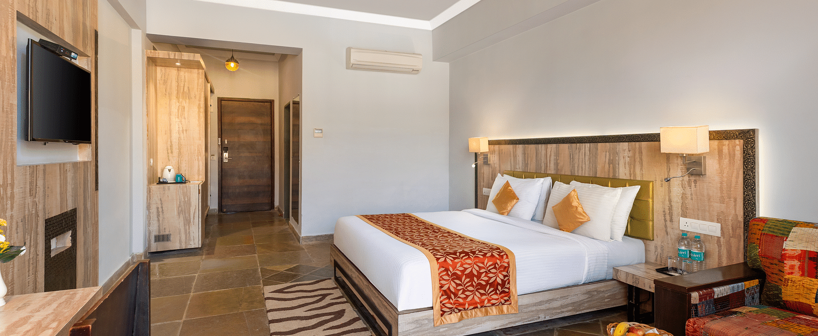 A hotel room with a bed, seating area, desk, TV, and a door leading to another room - Via Lakhela Resort & Spa, Kumbhalgarh
