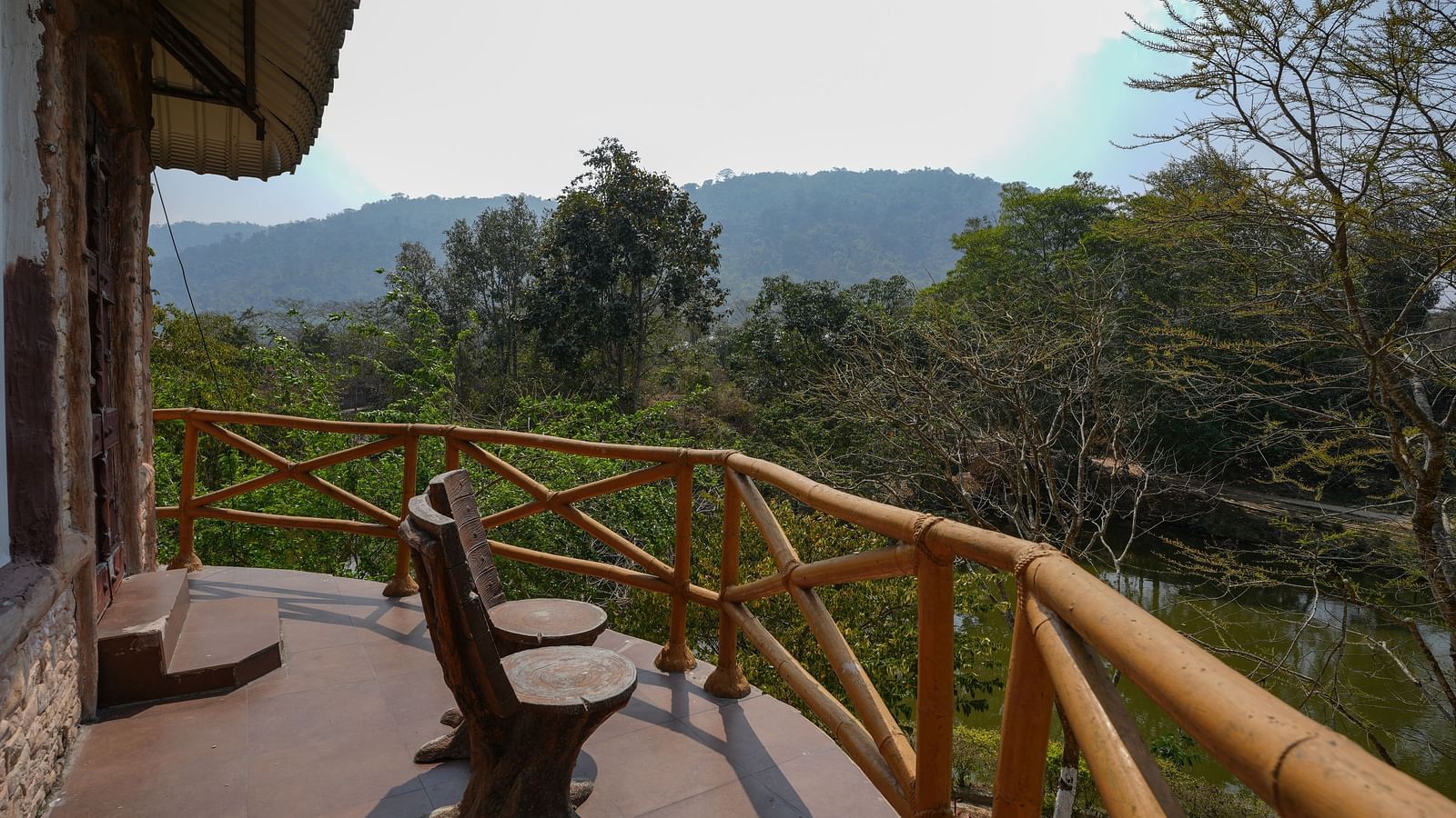 Ethnic villa offering a spacious balcony with tree-themed chairs for enjoying the lake & nature view at Summit Green Lake Tea Resort & Spa, Kazirang