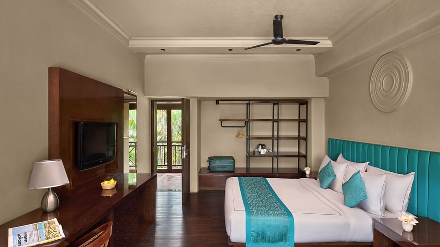 Executive Room with Balcony featuring a large bed, turquoise accents, and a window revealing a lush outdoor at DGV Resort by Treat, Silvassa