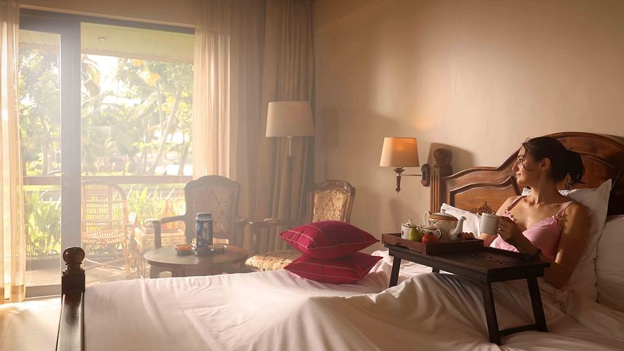 A woman relaxing in her room at Uday Backwater Resort, sipping hot beverage while gazing out the window.