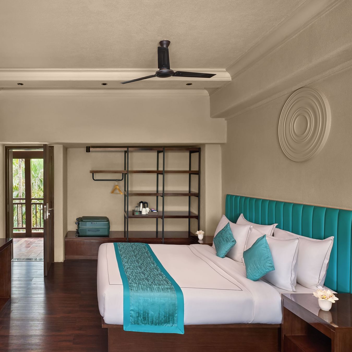 Executive Room with Balcony featuring a large bed, turquoise accents, and a window revealing a lush outdoor at DGV Resort by Treat, Silvassa