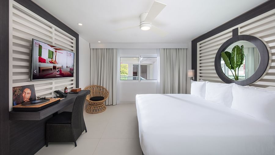 A hotel bedroom with a ceiling fan, a cushioned chair and a wall-mounted television - S Hotel Montego Bay, Jamaica