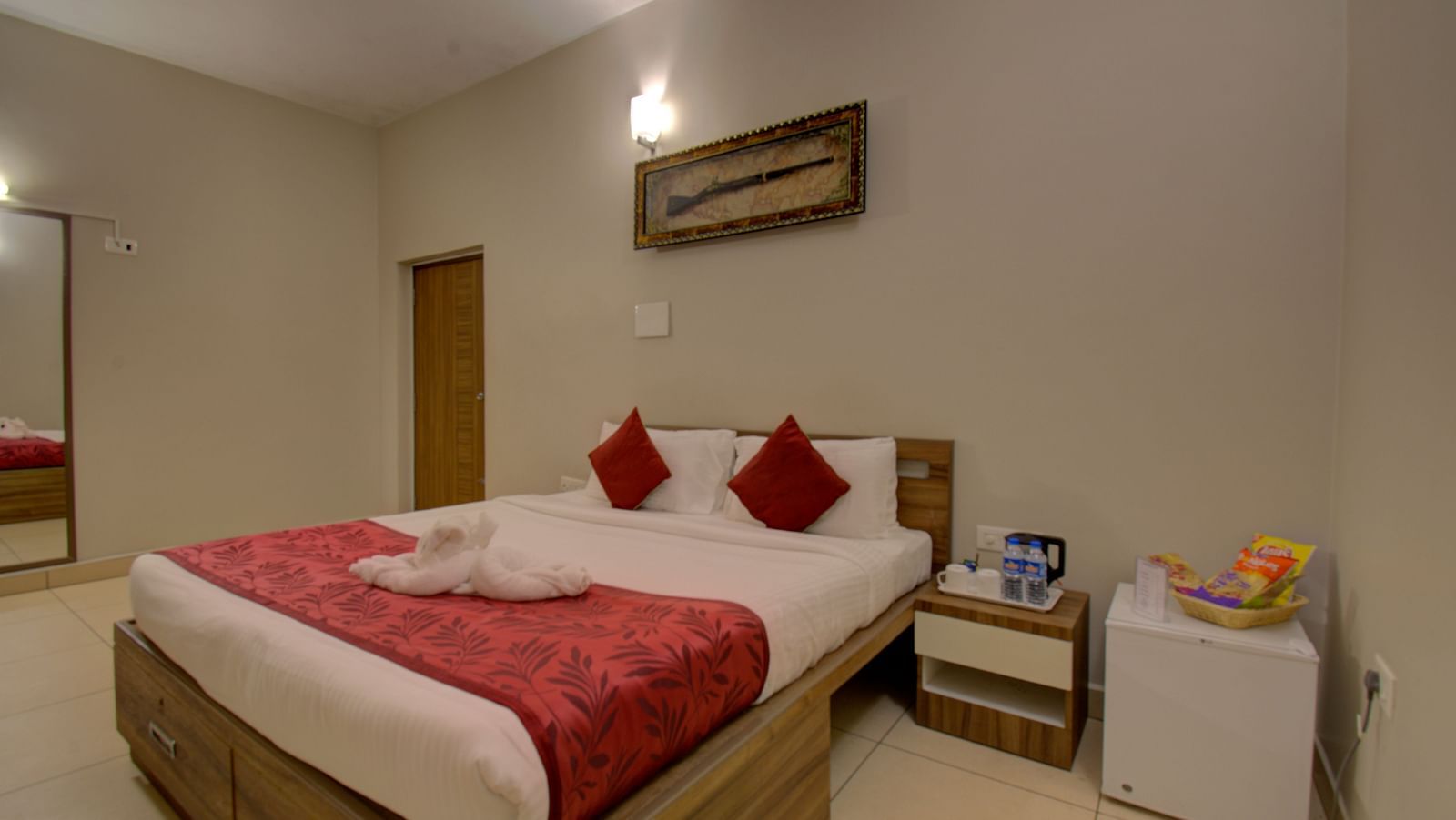 A swan made with of towel on a huge bed, a side table, mirror, wooden door and an wall art | Superior Room | Woodstock Resorts, Coorg