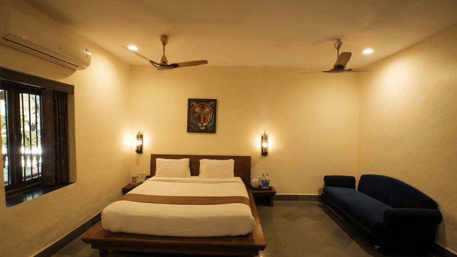 A bedroom at Adamo The Village with a multi-seating sofa, a window, wooden flooring, and 2 ceiling fans.