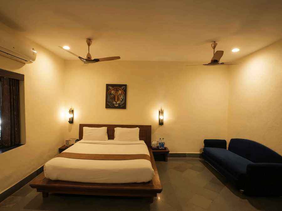 A bedroom at Adamo The Village with a multi-seating sofa, a window, wooden flooring, and 2 ceiling fans.