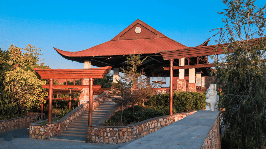 A Japanese-themed entry pavilion with a large structure, pathway and surrounding plants at Ananta Spa and Resort, Jaipur