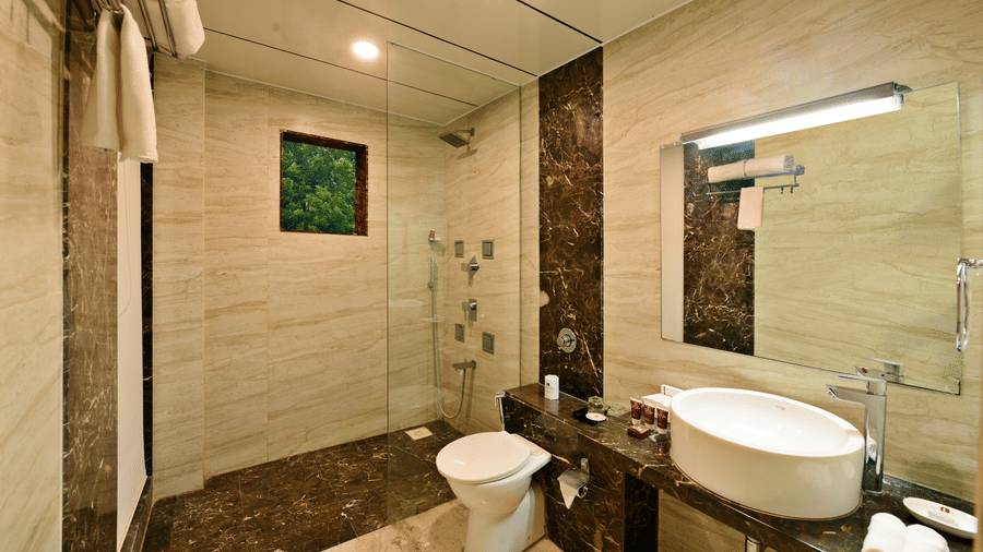 A well-lit hotel bathroom with a shower, toilet, and a modern sink vanity.
