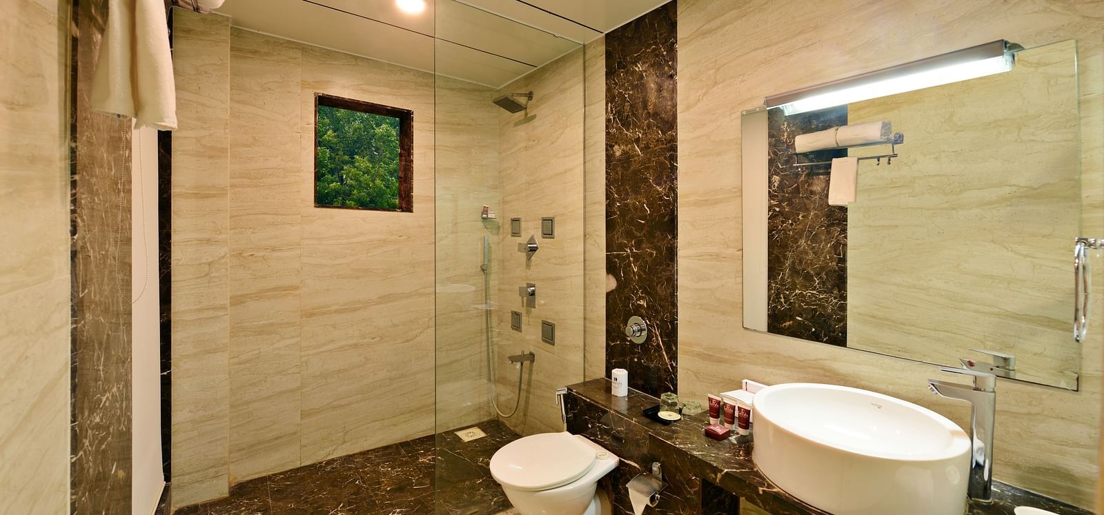 A well-lit hotel bathroom with a shower, toilet, and a modern sink vanity.